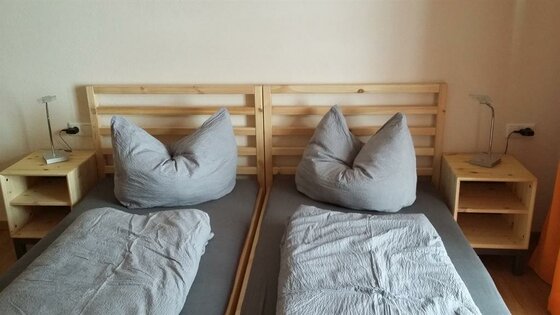 Schlafzimmer Biohof Foidl Zwei nebeneinanderstehende Holzbetten mit grauer Bettwäsche und Nachttischen.