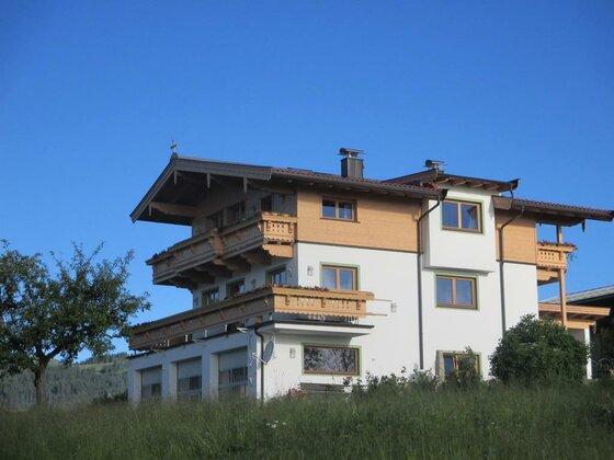Mehrstöckiges Alpenhaus mit Holzbalkonen und weißer Fassade vor blauem Himmel.