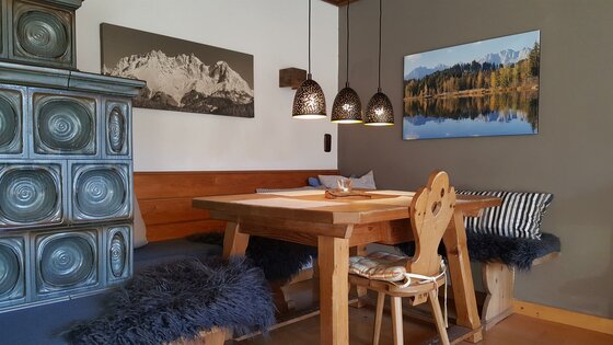 Sitzecke Ferienwohnung Wielemans Rustikale Sitzecke mit Holztisch, Eckbank, Kachelofen und drei Hängelampen in einer Ferienwohnung.