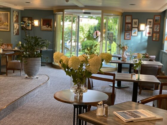 Innenansicht einer Hotel-Lounge mit Holztischen, Stühlen und Hortensien in einer Vase.