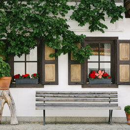 Zwei Fenster mit Blumen und einer Holzbank in einer charmanten Ecke in Kitzbühel.