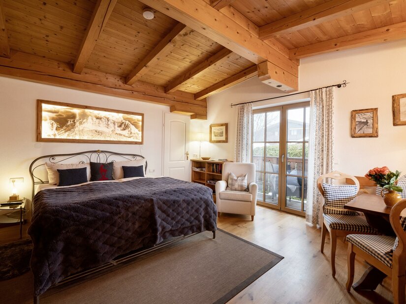 Das_Chalet_Kirchberger_Strasse_Kirchberg_Wohnraum Ein gemütliches Schlafzimmer mit einem großen Bett und Holzbalkendecke. Es gibt einen kleinen Essbereich und einen Balkon mit Blick nach draußen.
