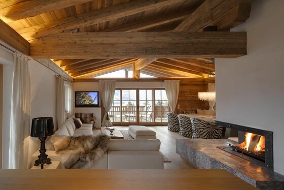 Moderner Wohnraum in einer Holzhütte mit Kamin, weißem Sofa und sichtbaren Dachbalken.
