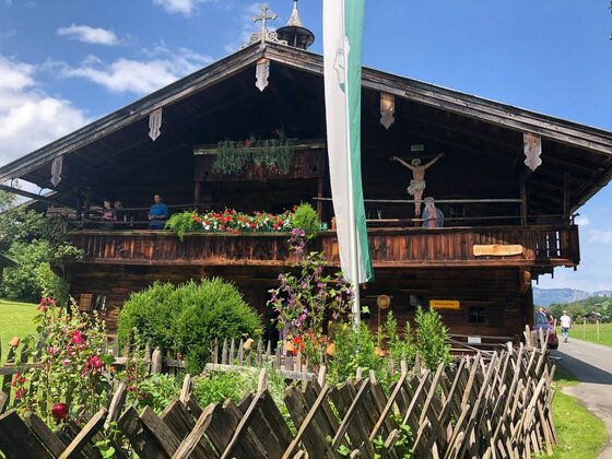 Historisches Bauernhaus am Museumsweg Traditionelles Bauernhaus aus dunklem Holz mit Blumenschmuck am Balkon und einem Holzzaun im Vordergrund.