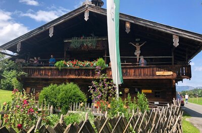 Historisches Bauernhaus am Museumsweg Traditionelles Bauernhaus aus dunklem Holz mit Blumenschmuck am Balkon und einem Holzzaun im Vordergrund.