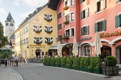 Hotel Tiefenbrunner in Kitzbühel Blick auf farbige Häuserfassaden mit Restaurants und einem Kirchturm im Hintergrund in einer gepflasterten Straße.