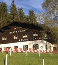 Zweistöckiges Holzgebäude mit weißem Erdgeschoss, roten Liegestühlen davor und einer österreichischen Flagge.