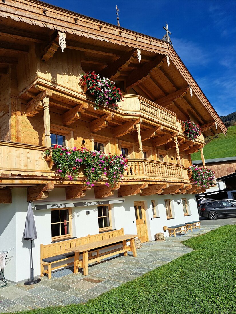 Ein traditionelles Holzhaus mit Blumenkästen an den Balkonen. Die grüne Wiese und der blaue Himmel sorgen für eine idyllische Atmosphäre.