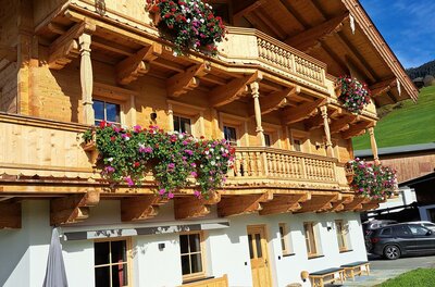 Ein traditionelles Holzhaus mit Blumenkästen an den Balkonen. Die grüne Wiese und der blaue Himmel sorgen für eine idyllische Atmosphäre.