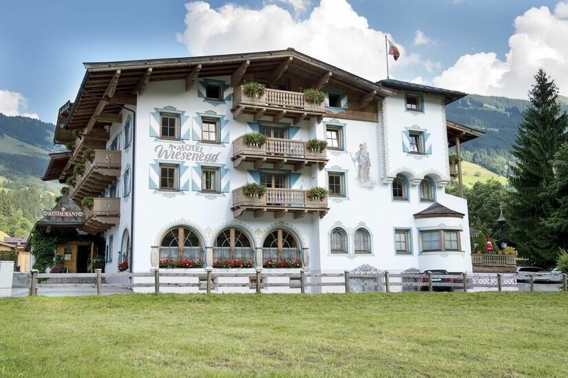Hotel Wiesenegg im Sommer Vorderansicht des Hotel Wiesenegg mit Holzbalkonen, Wandmalereien und grüner Wiese im Vordergrund.