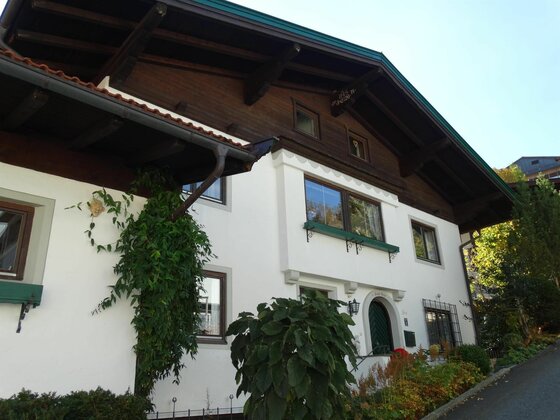 Zweistöckiges weißes Wohnhaus mit dunklem Holzdach und grünen Fensterläden.