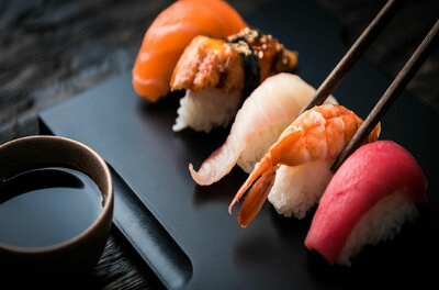 Rozu Sushi Bar Verschiedene Nigiri-Sushi auf einer schwarzen Platte mit Stäbchen und Sojasauce.