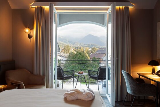 Hotelzimmer mit Bergblick Blick aus einem Hotelzimmer durch eine offene Balkontür auf Berge und Bäume.