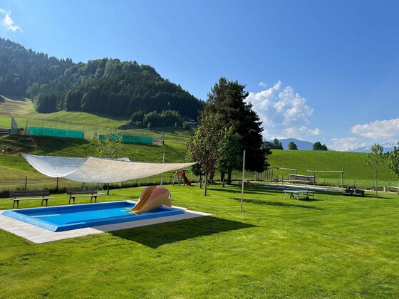 Schwimmbad Itter4 (c)ClarissaGünnewig Ein schöner Garten mit einem blauen Pool und einer Liegewiese. Im Hintergrund sind Hügel und ein klarer Himmel zu sehen.