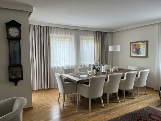 Moderner Essbereich mit großem Holztisch, weißen Polsterstühlen und einer antiken Standuhr an der Wand.