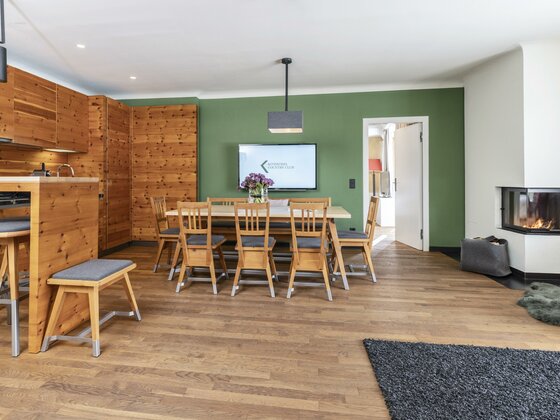 Moderner Essbereich mit Holztisch, grüner Wand, TV und Kamin in einer Ferienwohnung.
