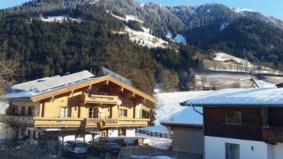 Haus Berger im Winter Alpines Holzhaus mit Solaranlage vor bewaldetem Berghang im Winter.