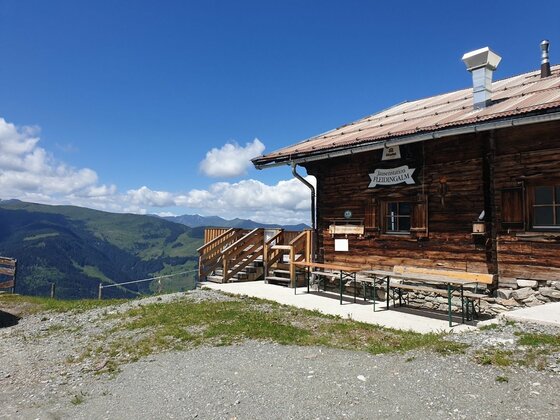 Berghütte Kandleralm Rustikale Holzhütte mit Sitzbänken vor Gebirgspanorama unter blauem Himmel.