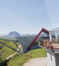 Moderne Bergstation mit Glaspavillon und Seilbahnstütze vor alpinem Panorama.