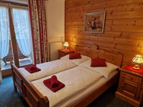 Doppelbett aus Holz in einem Zimmer mit holzgetäfelten Wänden und Balkonzugang.