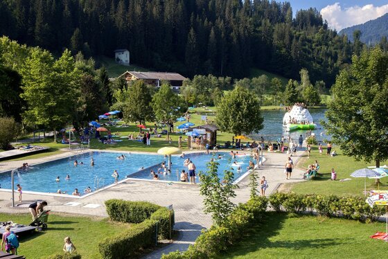 Schwimmbad @ Region Hohe Salve - Thomas Trinkl Ein wunderschöner Schwimmbereich mit zwei Becken und viel Grün. Menschen genießen die Sonne und das Wasser in einer ruhigen, naturnahen Umgebung.