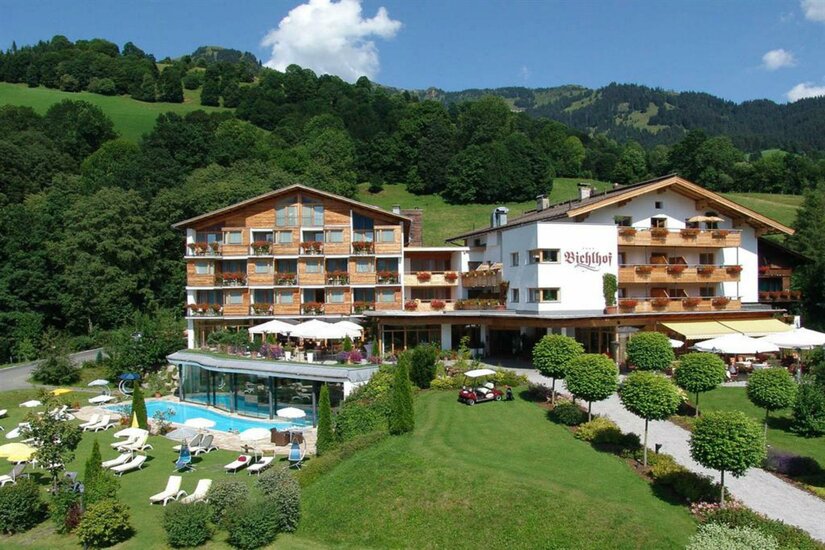 Hotel Bichlhof mit Außenanlage Alpines Hotelgebäude mit Außenpool, Liegewiese und bewaldeten Bergen im Hintergrund.