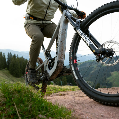 Ein E-Biker fährt in Kitzbühel über Steine, umgeben von grünen Wiesen und Bergen im Hintergrund.