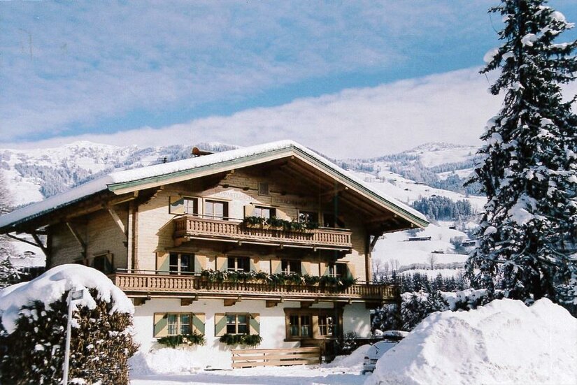 Auracherhof im Winter Alpines Holzhaus mit Balkonen im Schnee vor bewaldeten Bergen.
