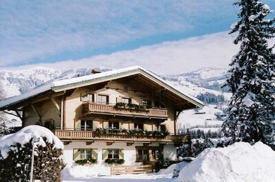 Auracherhof im Winter Alpines Holzhaus mit Balkonen im Schnee vor bewaldeten Bergen.