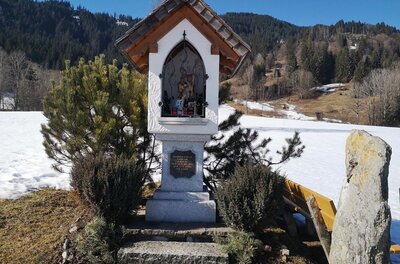 Bildstock bei Griesbach Ein weißer Bildstock mit Satteldach vor einer verschneiten Berglandschaft.