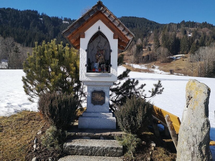 Bildstock bei Griesbach Ein weißer Bildstock mit Satteldach vor einer verschneiten Berglandschaft.