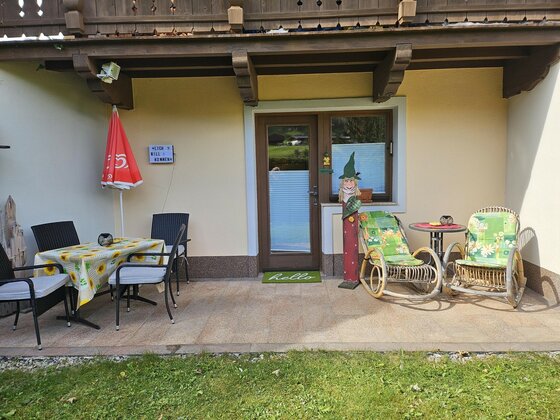 Gepflasterte Terrasse mit Esstisch, Stühlen und zwei Schaukelstühlen vor einer Hauswand.