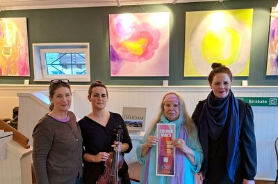 Eine Gruppe von vier Frauen steht in einer Kunstgalerie. Im Hintergrund sind bunte, abstrakte Gemälde zu sehen.