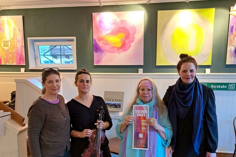 Eine Gruppe von vier Frauen steht in einer Kunstgalerie. Im Hintergrund sind bunte, abstrakte Gemälde zu sehen.