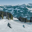Hahnenkamm bis Pass Thurn Winter 2018-19-07416 Zwei Skifahrer fahren über eine schneebedeckte Piste im Skigebiet Kitzbühel, umgeben von Bergen und Nadelwäldern.