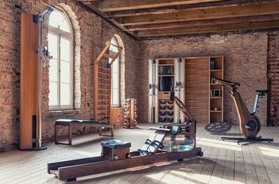 Bodyfit Fitnessraum Fitnessraum mit Holzgeräten, Rudermaschine und Ergometer vor einer Ziegelwand.