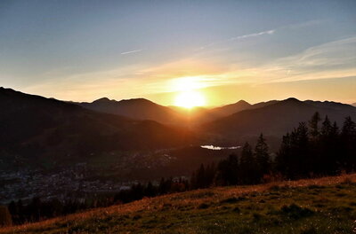 Blick von der Mittelstation Sonnenuntergang über einer bergigen Landschaft mit einem Tal und Nadelbäumen im Vordergrund.