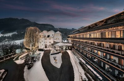 Ein charmantes Hotel in einer malerischen Winterlandschaft, umgeben von schneebedeckten Bergen. Die warme Beleuchtung der Fenster schafft eine einladende Atmosphäre.
