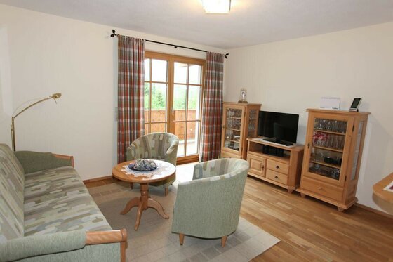 Wohnzimmer Oberhauser Wohnzimmer mit Sofa, zwei Sesseln, Holztisch und Vitrinenschränken vor einer Balkontür.