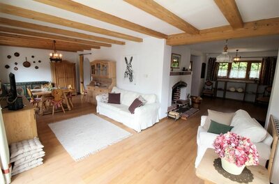 Wohnzimmer mit weißen Sofas, Holzbalkendecke, Kamin und Essbereich im Hintergrund.