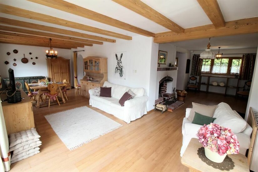 Wohnzimmer mit weißen Sofas, Holzbalkendecke, Kamin und Essbereich im Hintergrund.