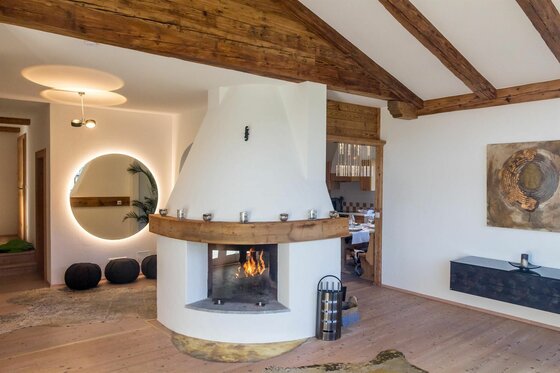 Wohnbereich Residenz am Berg Moderner Kamin in einem Wohnraum mit Holzbalkendecke und indirekt beleuchtetem Spiegel.