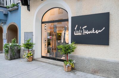 Luis Trenker Ladengeschäft Eingangsbereich eines Luis Trenker Bekleidungsgeschäfts mit Rundbogentür und schwarzem Firmenschild.