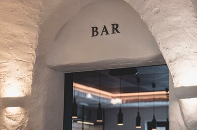 Eingangsbereich einer Bar mit Rundbogen und weißem Mauerwerk.
