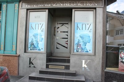 KitzMagazin Ein modernes Geschäft mit Glaseingang und auffälligen Werbeflächen. Die Fassade ist in Grautönen gehalten und zeigt das Logo "KITZ".