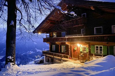 920F1AE6-0891-46B9-8EEE-7CDA3BAFB7F4_1_105_c Ein charmantes Holzhaus im Winter mit einer schneebedeckten Umgebung. Sanftes Licht strahlt aus dem Fenster und schafft eine gemütliche Atmosphäre.
