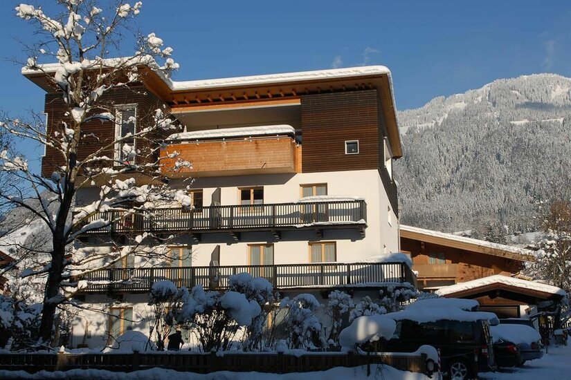 Gästehaus Maier im Winter Mehrstöckiges Gästehaus mit Holzbalkonen im Winter vor verschneitem Berghang.