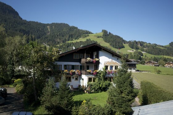 Alpines Gästehaus mit Blumenschmuck vor bewaldeten Bergen.