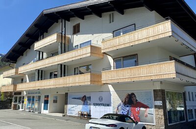 Mehrstöckiges Gebäude mit Holzbalkonen und Ladenzeile im Erdgeschoss in Kitzbühel.