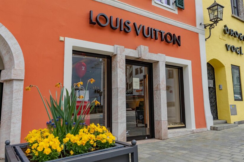 Louis Vuitton Boutique Außenansicht eines Louis Vuitton Geschäfts mit orangefarbener Fassade und gelben Blumen im Vordergrund.